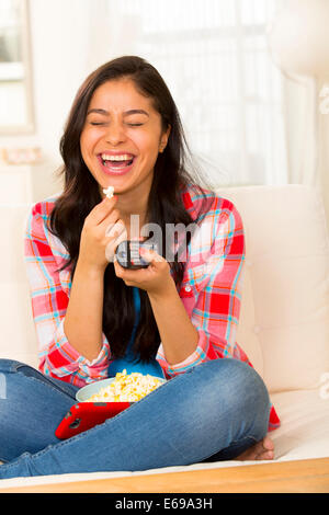 Hispanic woman eating popcorn on sofa Stock Photo