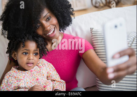 Mother taking photograph with daughter on sofa Stock Photo