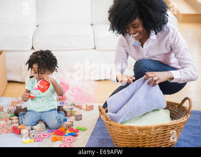 Mother folding laundry while daughter plays Stock Photo