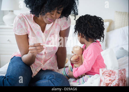 Mother checking daughter's temperature on bed Stock Photo