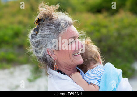 Caucasian woman carrying grandson on beach