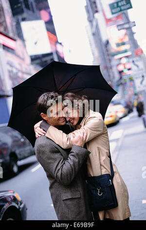 Couple huddled under umbrella on city street Stock Photo