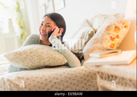 Mixed race teenage girl talking on cell phone on bed Stock Photo