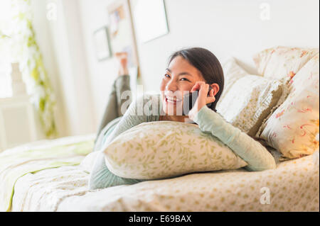 Mixed race teenage girl talking on cell phone on bed Stock Photo