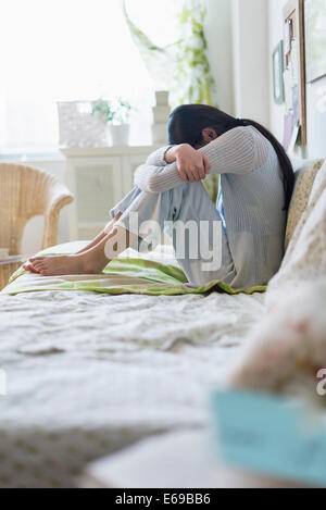 Mixed race teenage girl hugging her knees on bed Stock Photo