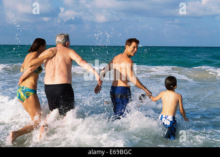 Family walking in waves on beach Stock Photo
