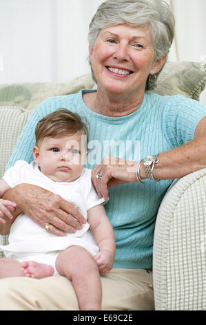 Senior woman sitting with granddaughter on sofa Stock Photo