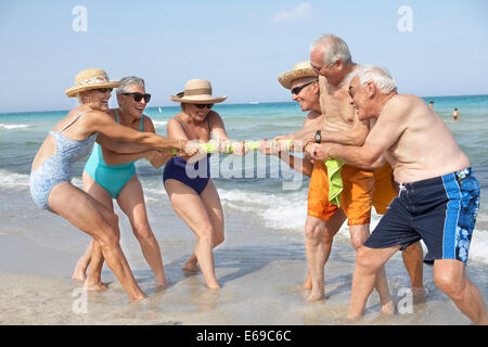 Senior friends playing tug-of-war on beach Stock Photo