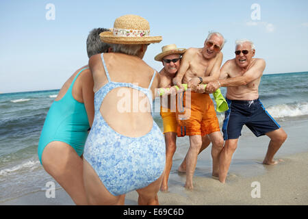 Senior friends playing tug-of-war on beach Stock Photo