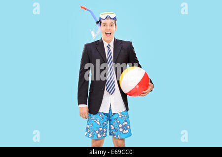 Excited businessman with a snorkel holding a beach ball on blue background Stock Photo