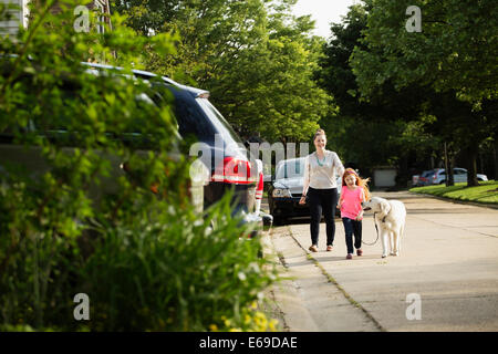 Caucasian mother and daughter walking dog on suburban street Stock Photo