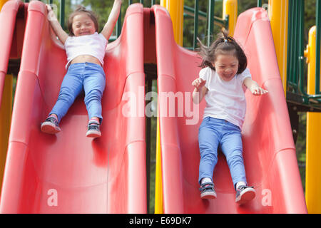 Mixed race Down syndrome girls playing on slides Stock Photo
