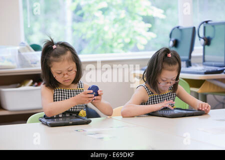 Mixed race Down syndrome students using tablet computers in classroom Stock Photo