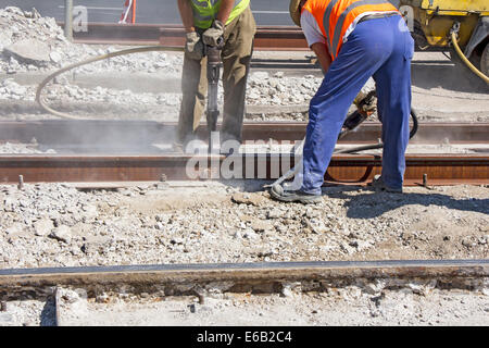 Two Workers with pneumatic hammer drill equipment breaking Concrete at construction site Stock Photo