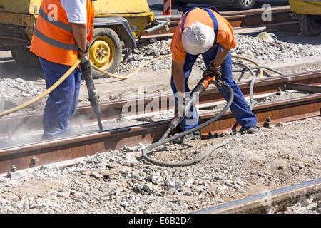 Two Workers with pneumatic hammer drill equipment breaking Concrete at construction site Stock Photo