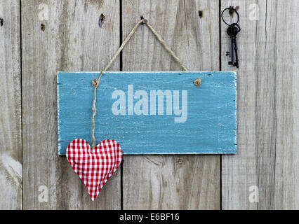 Blank antique blue sign with red checkered heart and iron keys hanging on distressed wood door Stock Photo