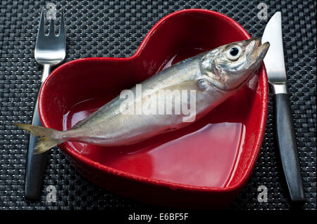 Fresh fish Tilapia Concept healthy eating with red heart shaped dish with knife and fork on black contemporary table Stock Photo