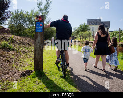 A cyclist passes a walking mother and two children on the coast to coast cycle route in Moor Row, Cumbria, England Stock Photo