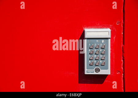 Close up of Bright red metal door with electronic combination entry entrance keypad lock England UK United Kingdom GB Great Britain Stock Photo