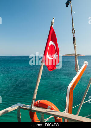 turkish flag on a hardwood mast flying at thhe stern rail of a wooden boat with green sea behind Stock Photo