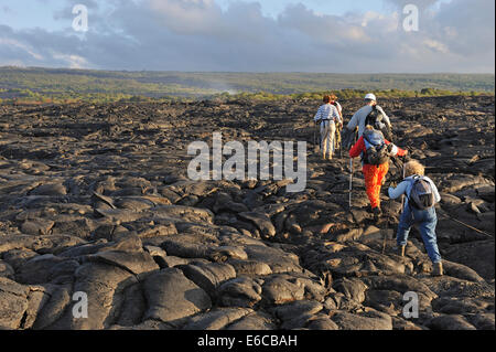 Group of hikers walking on cooled pahoehoe lava flow at sunrise, Kilauea Volcano, Big Island, Hawaii Volcanoes National Park, USA Stock Photo