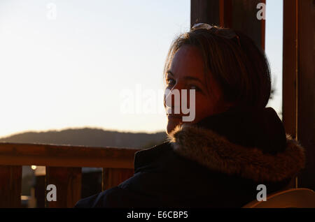 Woman sitting on a balcony in winter, looking at camera, outdoors at sunset Stock Photo