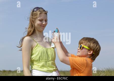 young boy spraying sunscreen into a teenage girl´s face, Scharbeutz, Baltic Sea, Schleswig-Holstein, Germany Stock Photo