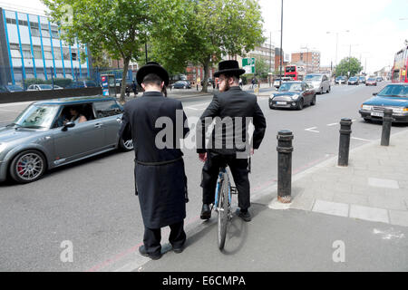 Orthodox Hasidic Jewish men with bicycle waiting to cross the road through traffic in Stamford Hill London N16  UK  KATHY DEWITT Stock Photo