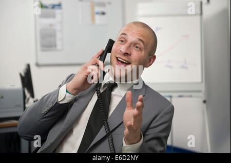 Young man wearing a suit is talking on a phone in the office Stock Photo