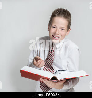 The smiling boy teenager in a white shirt and a tie reads a big red funny book Stock Photo