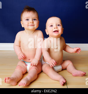 Fraternal twin 9 month old baby boys sitting side by side in their diapers Stock Photo