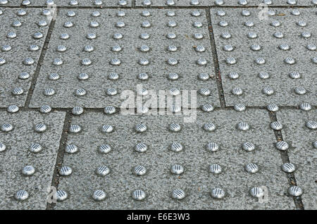 worn and bright stainless steel studs in natural gray paving flagstone to mark area of pavement for partially impaired crossing Stock Photo