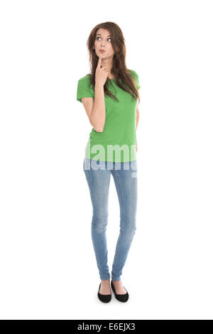 Slim young woman wearing green shirt and blue jeans in full body length looking pensive and amused up to the text. Stock Photo