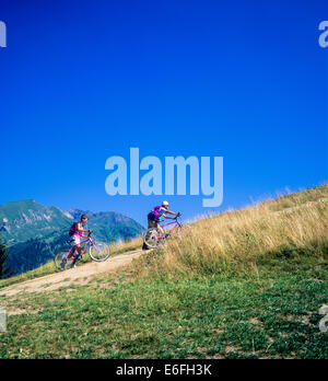 Couple of bikers pushing their mountain bikes to the top Morzine Savoy French Alps France Europe Stock Photo