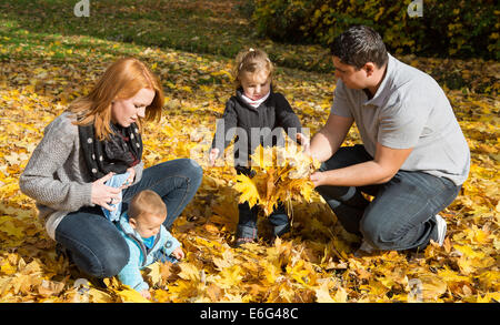 Happy young family in fall making a walk and play with maple leaves. Stock Photo