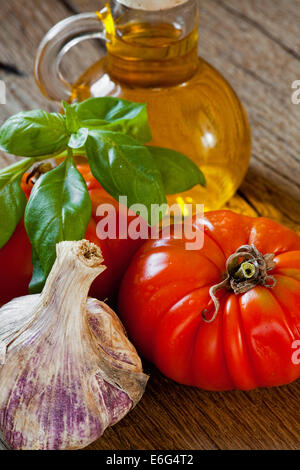 Freshly picked Beef tomatoes, basil, garlic and a bottle of olive oil on a rustic wooden table Stock Photo