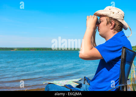 young man near the lake looking through binoculars Stock Photo