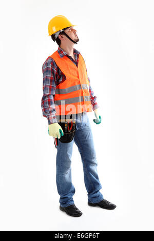 Serious construction worker in yellow helmet and orange waistcoat looking up. Full length studio shot isolated on white. Stock Photo