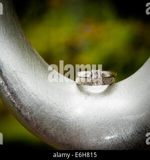 A white gold diamond engagement ring and wedding ring are displayed on a modern, silver curved object. Stock Photo