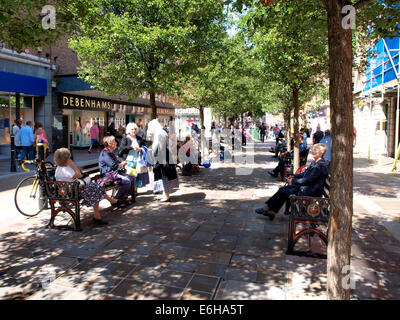 Shoppers resting on public benches in the shade of tree on a hot summers day, Worcester City Centre, UK Stock Photo