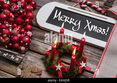 Merry christmas greeting card with four burning red candles and text on wooden sign. Stock Photo