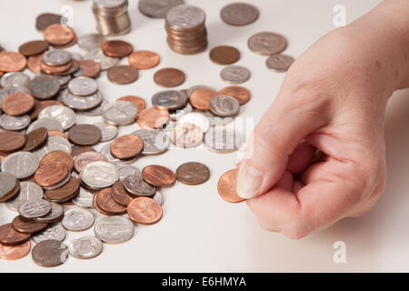 Woman's hand close up pinching a penny. Concept of retirement and not having enough money. Piles and stacks of coins ready for counting. Stock Photo