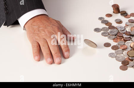 Man's hand flat on table after tossing spinning coin. Coin is stopped mid-spin with pile of coins beside it. Stock Photo