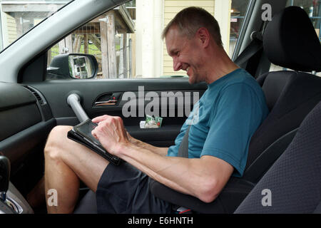 A man sat in a car using an ipad Stock Photo