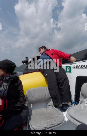 A photographer on a whale watching trip leaning far out of the boat, Tadoussac, Quebec Stock Photo