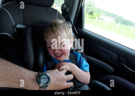 A man's hand tickling a baby in a car seat Stock Photo