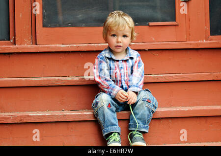 A young boy sat on the steps of a house undoing his laces