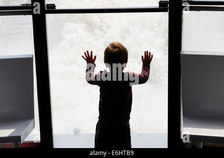 A young child in silhouette looking at the wake of a fast boat Stock Photo