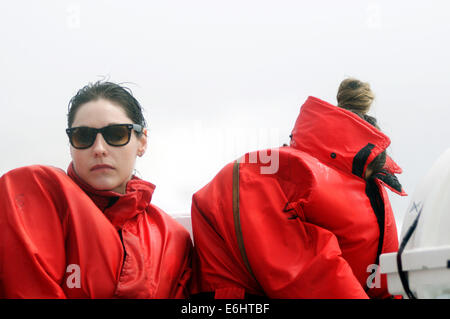 Two miserable women trying to hide from freezing cold spray on a whale watching boat ride on the St Lawrence Stock Photo
