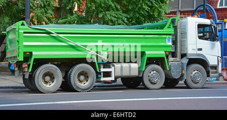 Side view unmarked clean green hgv tipper lorry truck & driver with dust cover in position driving along road in South London England UK Stock Photo